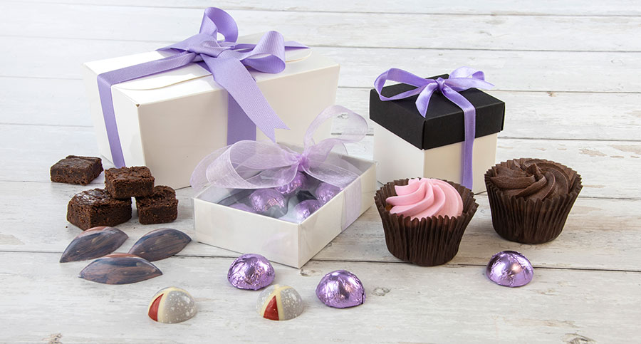 Display-of-white-packaging-of-different-sizes-and-shapes-with-lilac-decorations-containing-chocolates-buns-and-bakes